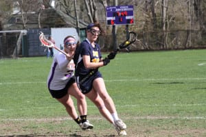 After winning the draw, Shoreham-Wading River’s Samantha Higgins maintains possession of the ball as she makes her way into Sayville’s zone with a defender on her hip, in the Wildcats’ 12-4 loss at Sayville Friday. Photo by Desirée Keegan