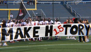 Newfield’s players stand behind a banner that reads "Let’s Make H15tory" which the Wolverines did, with a 41-33 win over MacArthur for the Class II Long Island championship title and the first undefeated season in program history on Nov. 27 at Hofstra University. Photo by Joe Galotti 