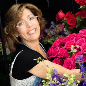 Debi Triola of Fashions in Flowers smiles with a floral arrangement. Photo from Triola