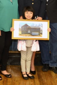 Lilianna Bonacasa, 5, holds up a photo of her family's new home given to them by the Rocky Point VFW Post 6249. Photo by Ron Pacchiana/JPA STUDIO