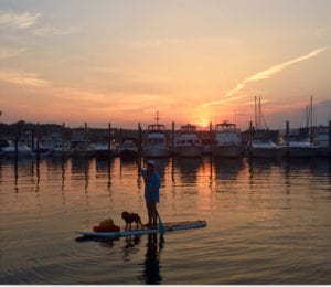 A woman and dog enjoy a paddleboarding ride during sunset. Photo from Katie Buttine