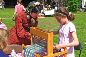 A volunteer and child practice on a loom at an event at the Huntington Historical Society. File photo 